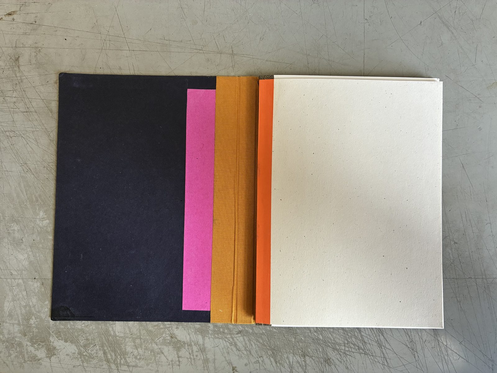 Carnet à cahiers permutables ouvert à plat : couverture bleu nuit, bande rose, dos en toile ocre, page crème