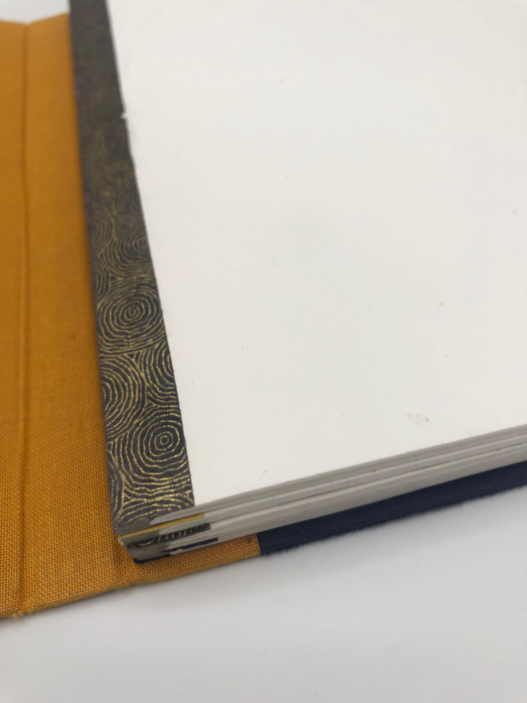 Détail du dos d’un cahier Flip Flap : papier japonais à spirales dorées, rabat de toile ocre