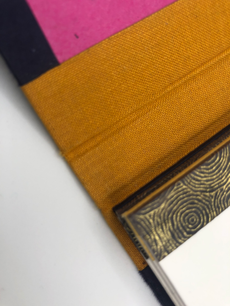 Détail Flip Flap : l’onglet de papier rose qui dépasse, la toile ocre et le dos doré en dessous